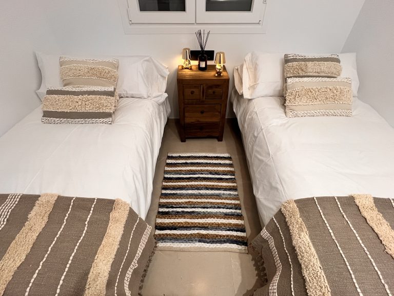 Dormitorio con camas separadas y alfombra central en Ático Suite Vejer