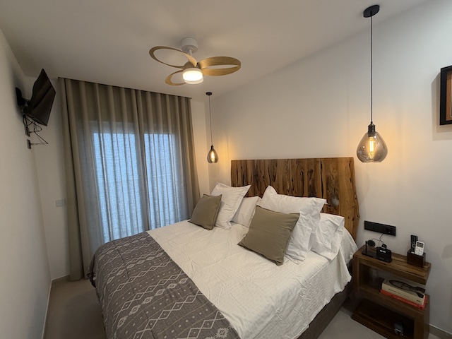 Habitación de matrimonio del ático en Vejer con cama doble, cabecero de madera, mesilla y cortinas.