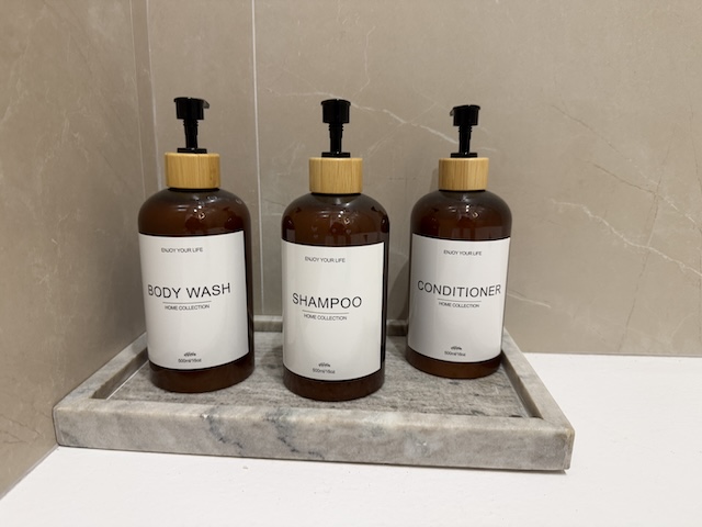 Botellas dispensadoras de gel, champú y acondicionador colocadas en bandeja dentro del baño.