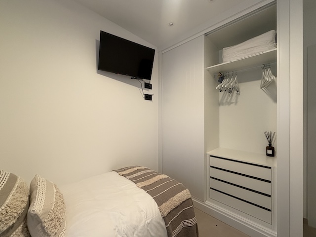 Interior de armario empotrado con perchas, estantes y cajonera blanca.