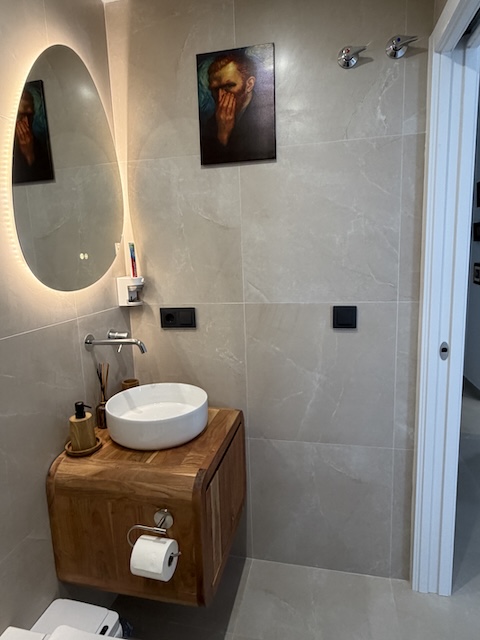 Distribución del baño pequeño con inodoro moderno y lavabo sobre mueble de madera suspendido.