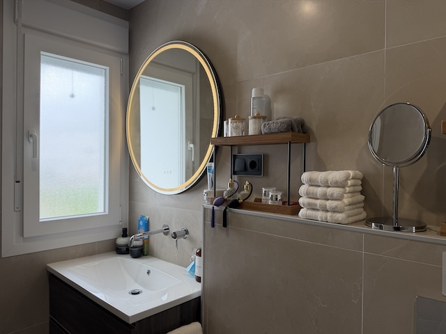 Vista amplia del lavabo con espejo retroiluminado y estanterías de amenities en baño principal.