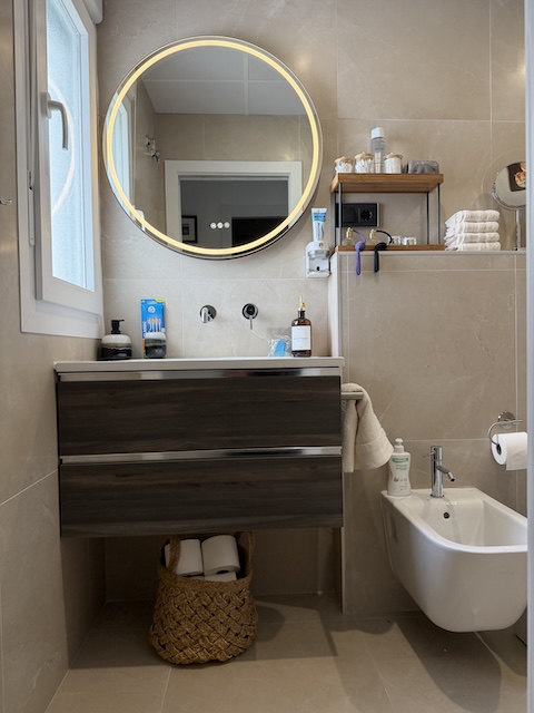 Mueble de lavabo moderno con espejo redondo iluminado en baño principal.