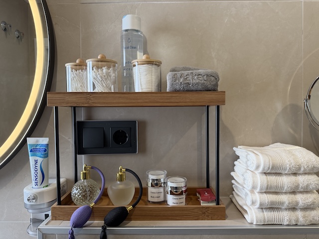 Estantería con algodón, bastoncillos, secador, cremas y toallas en baño principal.