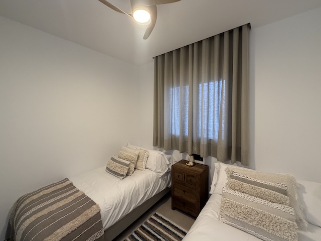 Habitación con dos camas individuales, mesita de madera y alfombra a rayas.