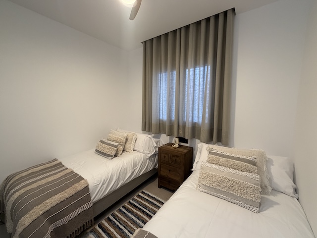 Dormitorio con dos camas individuales visto en ángulo, con ventana y cortinas.