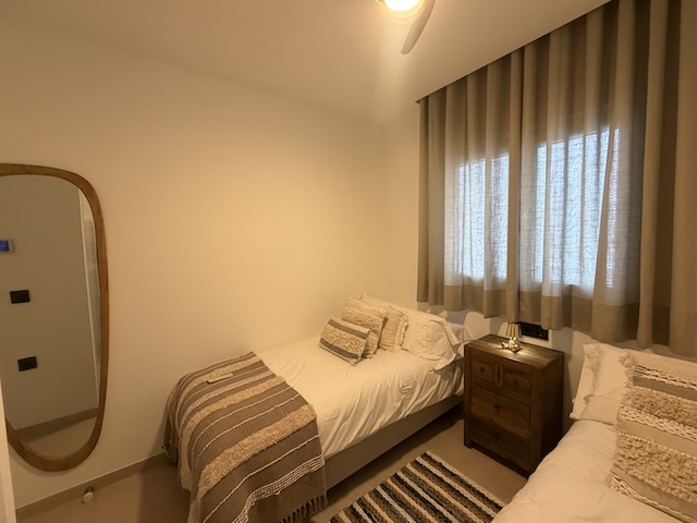 Dormitorio con dos camas individuales, espejo de cuerpo entero y mesita de noche bajo la ventana.