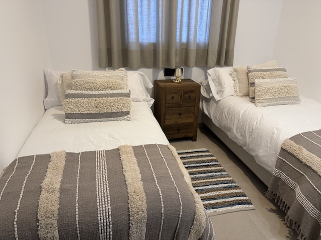 Dos camas individuales con mesita de madera y alfombra a rayas a los pies.