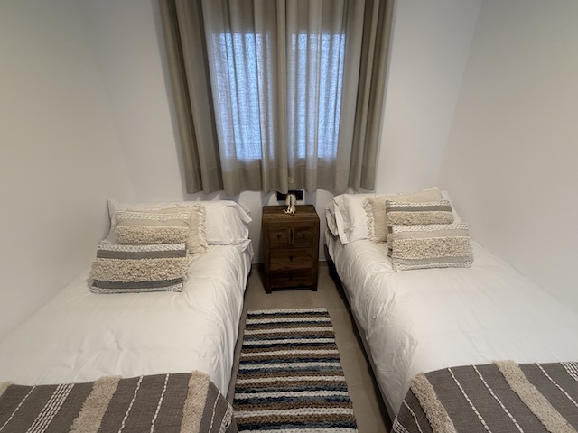 Vista del dormitorio desde los pies de cama con dos camas individuales y ventana.