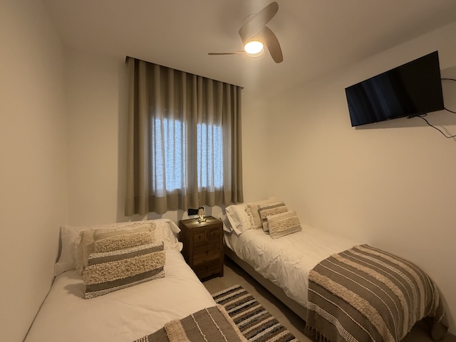 Dormitorio luminoso con dos camas individuales, cortinas y ventilador de techo.