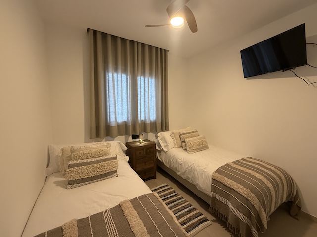 Dormitorio con dos camas individuales, TV en pared y ventilador de techo.