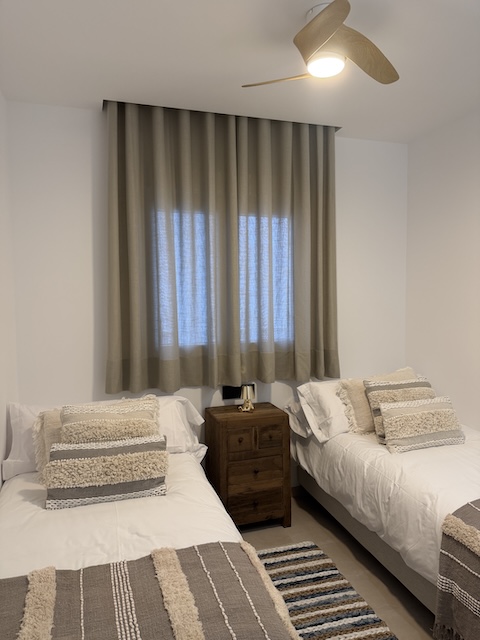 Habitación con dos camas individuales, ventana con cortinas y ventilador de techo.