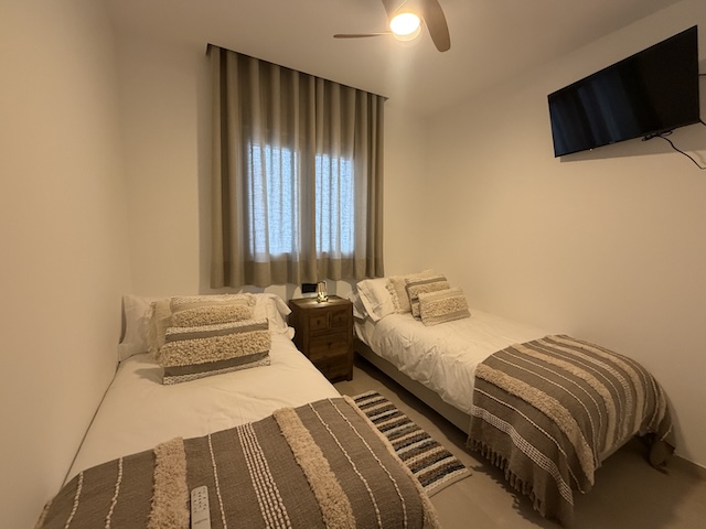 Habitación con dos camas individuales, mesita central y TV de pantalla plana.