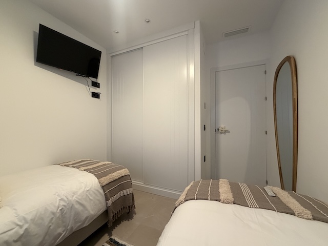 Dormitorio con TV en pared, armario empotrado blanco y espejo de cuerpo entero.