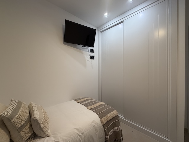 TV en pared y armario empotrado de puertas correderas en dormitorio.