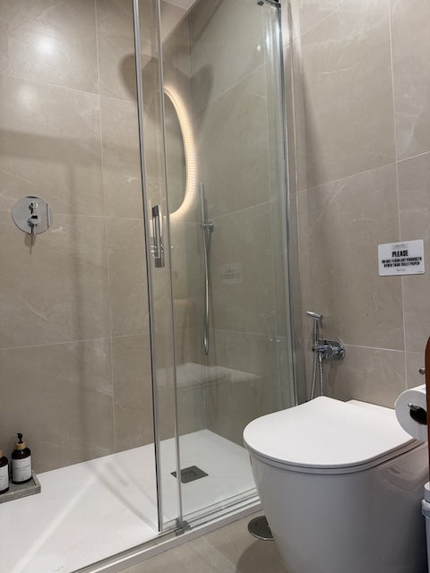 Ducha con mampara de cristal, plato de ducha blanco y desagüe lineal en baño moderno.