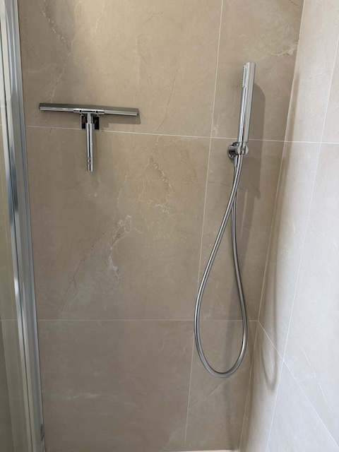 Ducha de mano con barra cromada en la ducha principal del baño.