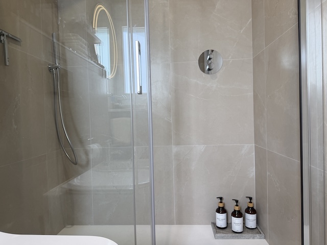 Interior de la ducha con mampara y amenities en un rincón de apoyo.