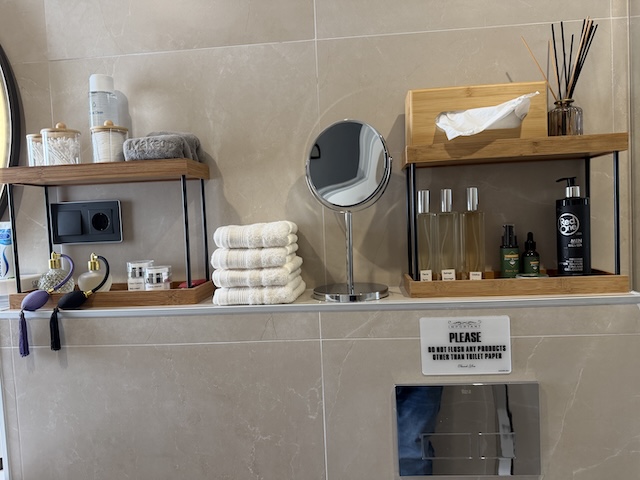 Estanterías con espejo de aumento, toallas dobladas y detalles decorativos en baño principal.