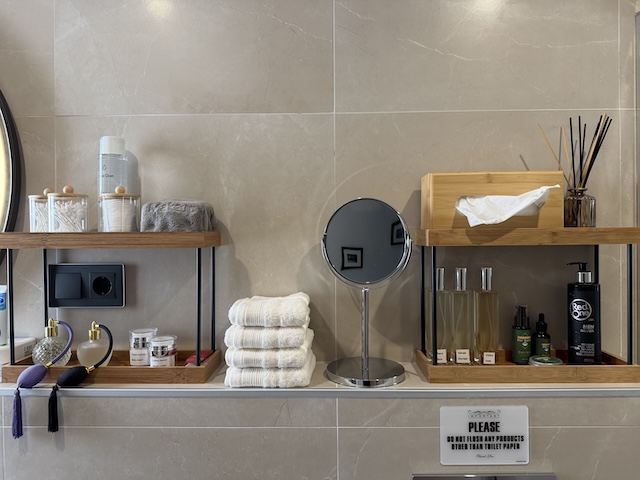 Estanterías con toallas, pañuelos, espejo de aumento y amenities en baño principal.