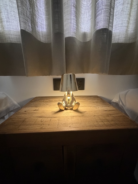 Lámpara encendida sobre mesita de madera con cortinas al fondo.