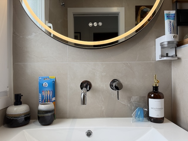 Lavabo con dispensador de jabón, artículos de cortesía y espejo retroiluminado en baño principal.