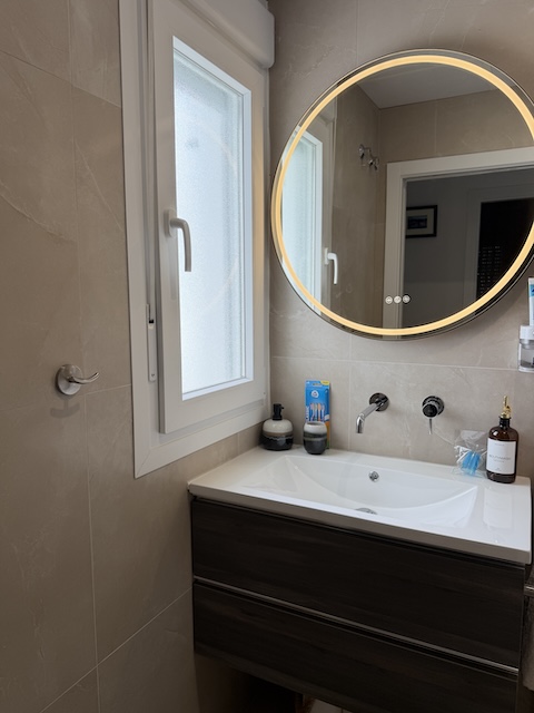 Lavabo del baño principal con espejo redondo retroiluminado, grifería empotrada y ventana.