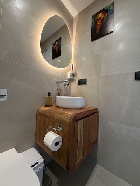 Lavabo blanco sobre mueble de madera con espejo retroiluminado en baño pequeño moderno.