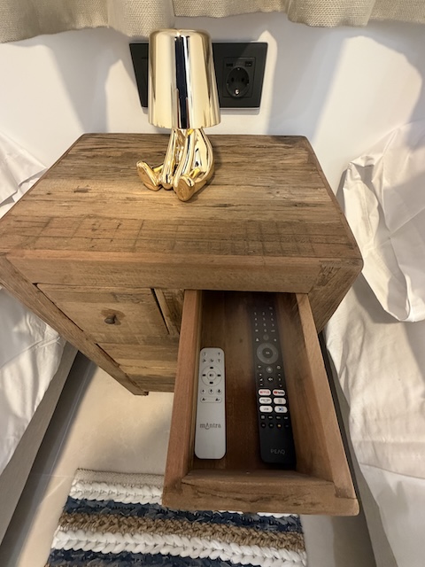 Mesita de noche de madera con lámpara y cajón con mandos a distancia.